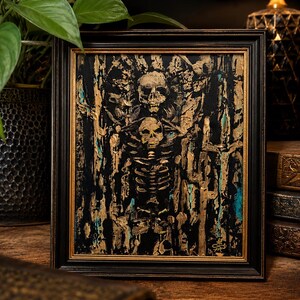 May include: A framed painting featuring a central skeleton figure with a skull head, rendered in thick, textured gold and black paint. The background consists of vertical, abstract strokes of gold, black, and teal, all enclosed in a black frame.