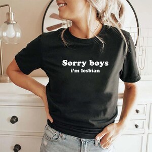 May include: Black t-shirt with the text "Sorry boys i'm lesbian" in white. The shirt is a crew neck style and is made of a soft material. The text is centered on the chest.