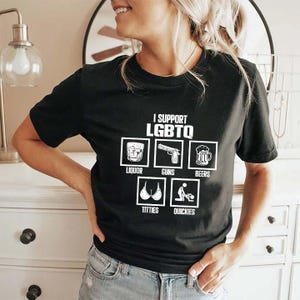 May include: Black t-shirt featuring the text "I SUPPORT LGBTQ" and images of liquor, guns, beers, titties, and quickies. The shirt is made of a soft material and is suitable for casual wear.