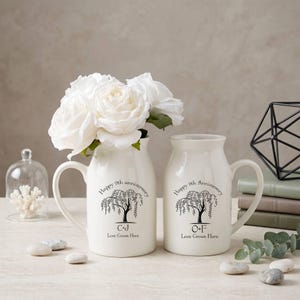 Puede incluir: Dos jarrones de cerámica blanquecina con asas, uno lleno de rosas blancas. Cada jarrón tiene un diseño de sauce llorón negro y el texto "Happy 9th anniversary" y "Love Grows Here". Los jarrones están personalizados con iniciales.