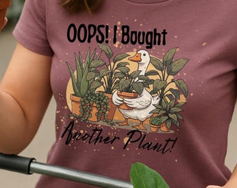 May include: A maroon t-shirt with the text "OOPS! I Bought Another Plant!" and a graphic of a duck with plants. The image shows a person holding a potted plant and pushing a shopping cart with more plants.