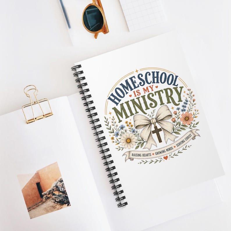 May include: A spiral-bound notebook featuring a graphic with the text "HOMESCHOOL IS MY MINISTRY" in blue and green, accompanied by a large beige bow, a cross, floral illustrations, and a banner reading "RAISING HEARTS GROWING MINDS SERVING CHRIST."