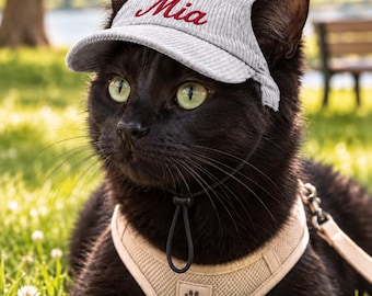 May include: A light gray corduroy baseball cap with the name Mia embroidered in red script, featuring a black chin strap. The cap is worn by a black cat wearing a beige mesh harness with a paw print patch and a leash. Text reads 8 Unique Retro Designs.