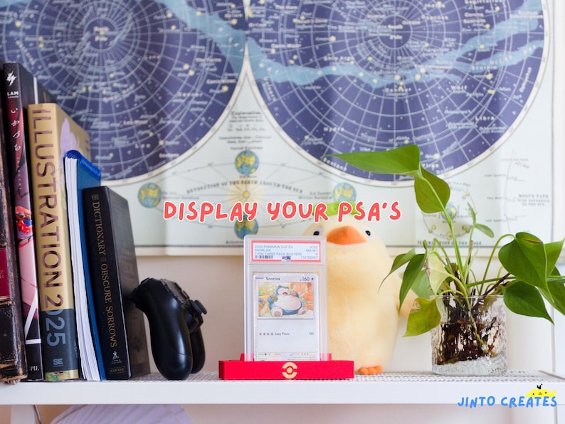 May include: A shelf with books, a games controller, and a plush duck. A graded trading card is displayed in a red stand. The text "DISPLAY YOUR PSA'S" is visible on the wall.