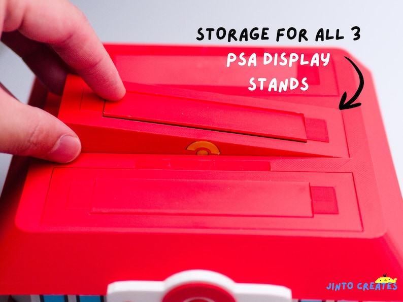 May include: A red plastic storage container with the text "STORAGE FOR ALL 3 PSA DISPLAY STANDS". The container has three angled slots for display stands. A hand is interacting with the container.