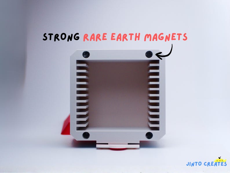 May include: A light grey rectangular object with vertical lines on the sides. The text "STRONG RARE EARTH MAGNETS" is written above the object. Four black magnets are visible on the corners of the object.