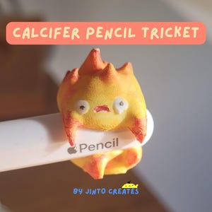 Peut inclure: Un accessoire de crayon Calcifer jaune et orange, un petit démon de feu de dessin animé, est fixé à un crayon blanc. Le tricket a une expression surprise. Le texte "CALCIFER PENCIL TRICKET" est dans une bannière pêche.