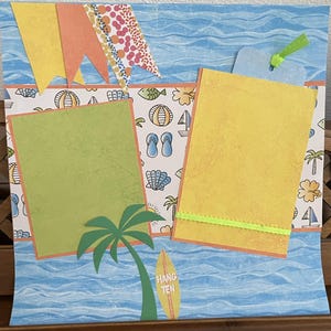 May include: A scrapbook page with a beach theme. It features a blue background with wavy lines, a palm tree, and a surfboard that says "Hang Ten." There are two photo mats, one green and one yellow, and decorative elements like pennants and beach-themed illustrations.