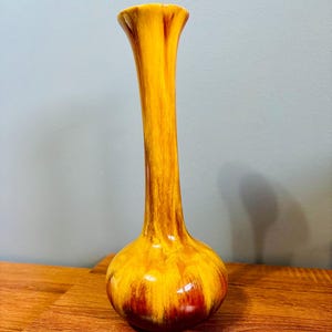 Puede incluir: Un jarrón alto y esbelto con base bulbosa y parte superior acampanada. El jarrón de cerámica presenta un acabado brillante con una mezcla de tonos amarillos, naranjas y marrones. El jarrón mide aproximadamente 30 cm de alto, perfecto para exhibir flores.