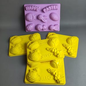 May include: A collection of Easter-themed molds in purple and yellow. The purple mold has the words "Happy Easter" and Easter-related shapes. The yellow molds have Easter-themed shapes and the words "Celebrate Spring".