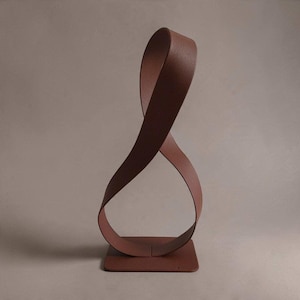 May include: A brown metal sculpture featuring a single continuous ribbon-like band that twists into a vertical loop. The structure is mounted on a flat, square base, creating a fluid, open form with a matte, textured finish throughout.