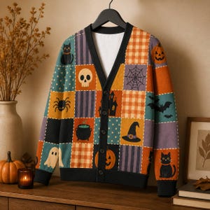 以下が含まれることがあります： ハロウィーンをテーマにした正方形のパッチワーク柄が特徴の、長袖ボタン付きカーディガン。黒猫、ドクロ、クモ、大釜、幽霊、魔女の帽子、カボチャ、コウモリ、お化け屋敷のイラストが描かれています。