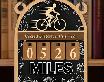 May include: Wooden cycling log sign with a chain for hanging. The sign features a cyclist graphic, the text "Cycled Distance This Year," and a counter displaying "0526 MILES." The sign is personalized with "Jack's Cycling Log."