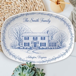 Puede incluir: Plato ovalado para servir con una ilustración azul y blanca de una casa, árboles y un borde floral. El texto "The Smith Family" y "Arlington, Virginia" se muestran en el plato. El plato está sobre una superficie blanca.