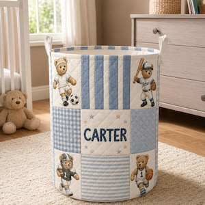 Può includere: Un contenitore cilindrico in tessuto con motivo trapuntato a righe e quadretti vichy blu e bianchi. Presenta orsetti ricamati che giocano a calcio, baseball, football americano e basket, con il nome CARTER ricamato in blu.