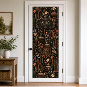 Op de afbeelding: Een witte deur met een verticale rechthoekige muursticker op een zwarte achtergrond, voorzien van een dicht patroon van kleurrijke bloemen en stapels oude boeken. De tekst "Olivia's READING NOOK" staat in het midden in goud.