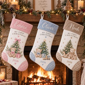 Peut inclure: Trois chaussettes de Noël personnalisées avec un corps blanc, un revers et un talon colorés. Elles portent les prénoms Emma, Oliver et Noah, le texte My First Christmas, un ours en peluche, un sapin de Noël et l'année 2026.