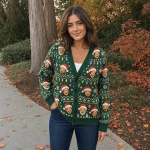 May include: A dark green V-neck cardigan featuring a repeating knit pattern of colorful Christmas lights, white snowflakes, and multiple cartoon faces wearing red Santa hats, secured with a row of dark buttons down the center front.