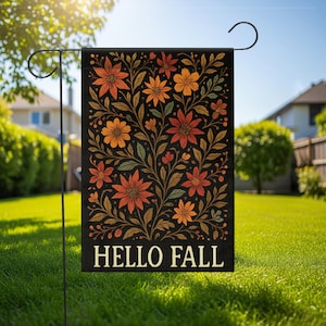 Puede incluir: Bandera de jardín negra con un diseño floral en tonos naranja, rojo y amarillo, con hojas verdes. Las palabras "HELLO FALL" están impresas en blanco en la parte inferior. La bandera está colgada en un soporte de metal negro en un jardín.