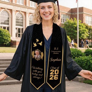 May include: A graduate in a black gown and cap, smiling, wearing a custom black and gold graduation stole. The stole has a photo, doves, and the text "Walking with you today and always!" and "Class of 2026".