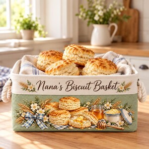 May include: A rectangular fabric storage basket with rope handles, featuring the text Nana's Biscuit Basket. The exterior is decorated with illustrations of wheat, white flowers, a blue gingham bow, and biscuits with honey.