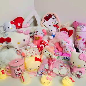 Può includere: Una collezione di articoli di Hello Kitty, tra cui peluche, una tazza, una borraccia, un portamonete e luci decorative. Gli articoli sono principalmente rosa e bianchi, con fiocchi rossi e il personaggio di Hello Kitty.