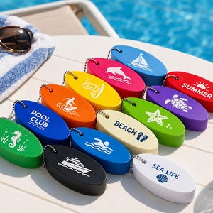 May include: A collection of oval-shaped foam keychains in various colors including red, orange, yellow, green, blue, black, and white. Each keychain features a white graphic print such as a sailboat, dolphin, turtle, starfish, seahorse, yacht, or text.