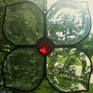 May include: A stained glass windowpane in the shape of a flower with four petals. The petals are clear glass with a slight blue tint. The center of the flower is a red glass circle.