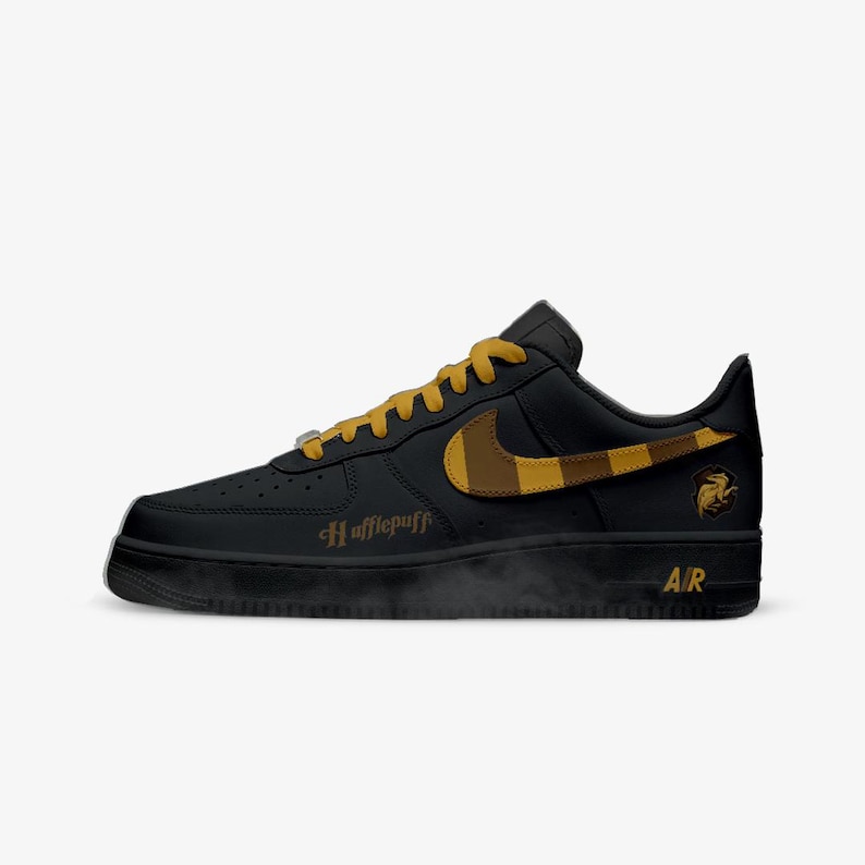 May include: Black and gold Nike Air Force 1 sneakers with Hufflepuff details. The shoe features a black base with gold accents, including the Nike swoosh, laces, and the Hufflepuff crest. The word "Hufflepuff" is printed on the side.
