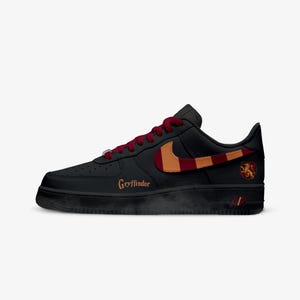 May include: Black Air Force 1 sneakers with a red and gold design. The Nike swoosh is red and gold. The word "Gryffindor" is written in gold on the side of the shoe. A Gryffindor crest is on the heel.