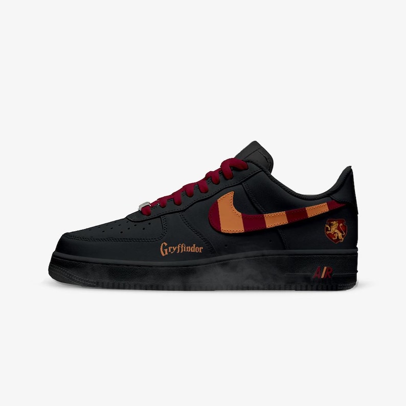 May include: Black Air Force 1 sneakers with a red and gold design. The Nike swoosh is red and gold. The word "Gryffindor" is written in gold on the side of the shoe. A Gryffindor crest is on the heel.