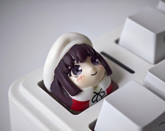 May include: A custom keycap featuring a cartoon character's head, with dark purple hair, a white hat, and a red and white outfit. The keycap is designed to fit on a mechanical keyboard, and is set between white keys.