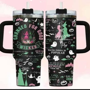 K&ouml;nnte beinhalten: Ein schwarzer Reisebecher mit Griff und Strohhalm. Der Becher ist mit einem "Wicked"-Thema verziert, das Silhouetten von Hexen, Geistern und S&auml;tzen wie "Changed for Good" und "You're Gonna Be Popular" zeigt.