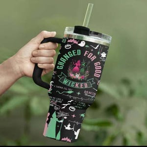 K&ouml;nnte beinhalten: Schwarzer Becher mit schwarzem Griff und transparentem Deckel, mit dem Text "Changed for Good" und "Wicked". Der Becher hat ein gr&uuml;n-rosa Farbverlauf am Boden und ist mit Hexen-Grafiken verziert.