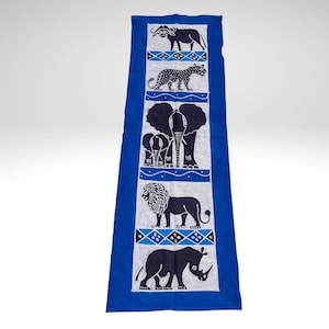 Può includere: Un runner rettangolare in tessuto blu con un pannello centrale bianco caratterizzato da illustrazioni stampate in nero di un bufalo, un leopardo, un elefante, un leone e un rinoceronte, separati da fasce orizzontali con motivi geometrici blu e bianchi.