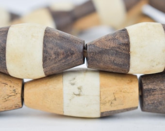 May include: Close-up of a strand of wooden beads. The beads are barrel-shaped with alternating sections of dark brown and cream-coloured wood. The beads are strung together, creating a textured and natural aesthetic.