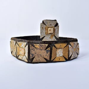 May include: An antique, decorative belt with a matching square centerpiece. The belt is dark brown with gold and silver-colored square accents. The centerpiece is a smaller version of the belt's design, with a square center.