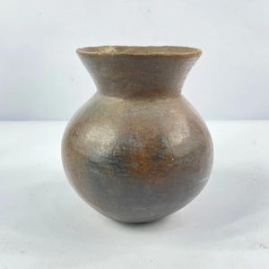 Peut inclure: Un vase en céramique marron fait à la main, avec un corps arrondi et un bord évasé. Le vase a un aspect rustique avec des variations de couleur, allant du marron foncé aux nuances plus claires. Le récipient est probablement utilisé à des fins décoratives.