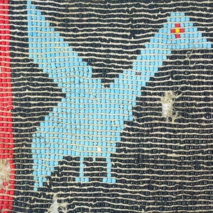以下が含まれることがあります： 蝶のデザインが施されたビーズ織物のクローズアップ。蝶は黒い背景に水色です。左側には赤いストライプがあります。織物は小さなビーズで作られています。