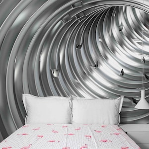 Puede incluir: Dormitorio con un diseño de pared futurista, plateado y metálico. La cama tiene almohadas blancas y una colcha con estampado de flamencos. Una mesita de noche blanca y una lámpara colgante completan la estética moderna.