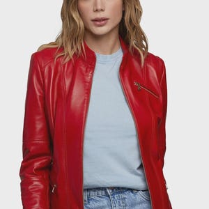 May include: A vibrant red leather jacket with a zip-up front and a stand-up collar. The jacket features vertical seams and a small zippered pocket. The model is wearing a light blue t-shirt underneath. The jacket is a classic outerwear piece.