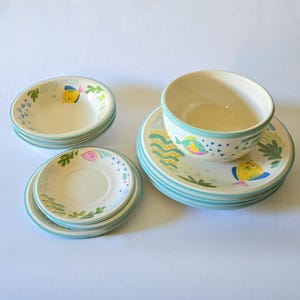 May include: A set of ceramic tableware featuring a whimsical aquatic theme. The set includes small bowls, saucers, and a larger bowl, all adorned with colorful fish, seaweed, and wave designs. The rims are painted in a light blue color.