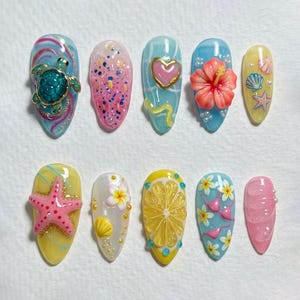 May include: A set of ten press-on nails featuring tropical and summer themes. Designs include a 3D sea turtle, pink glitter, a heart, a hibiscus flower, seashells, a starfish, a lemon slice, a bikini, and floral patterns in blue, pink, and yellow.