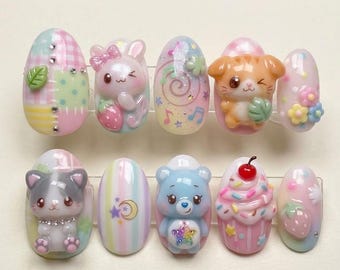 May include: A set of ten press-on nails in pastel shades. The designs include cartoon animals, strawberries, musical notes, and a cupcake. The nails are decorated with 3D embellishments and feature colours like pink, blue, and yellow.