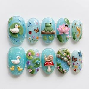 May include: A set of ten artificial nails with a light blue water-themed design. Each nail features a different miniature 3D element, including ducks, a frog, a snail, a lotus flower, and a koi fish. Other elements include butterflies, dragonflies, and lily pads.