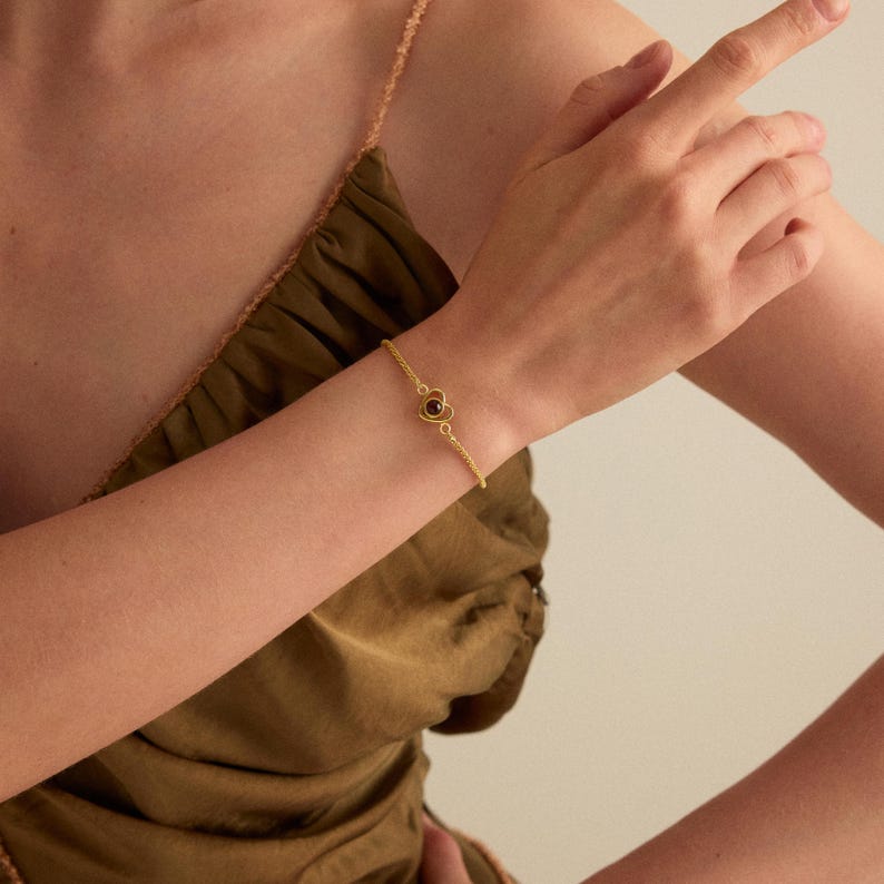 May include: A gold-colored bracelet with a four-leaf clover design and a dark brown center stone. The bracelet is worn on a person's wrist, and the background is a solid color.