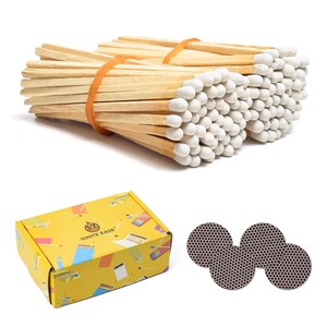 May include: Two bundles of wooden matches with white tips, secured by orange rubber bands. A yellow rectangular box with the text IGNITE EASE and various match-themed illustrations. Three circular dark brown textured match-striking pads.