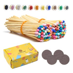 May include: Two bundles of wooden matches with multi-colored heads secured by orange rubber bands, a yellow rectangular box with the text IGNITE EASE and match illustrations, and three circular dark brown textured match striking pads.