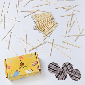 May include: A collection of wooden matches with white tips scattered on a white surface. A yellow box with the text "IGNITE EASE" and a flame logo is visible, along with three circular match strike pads.