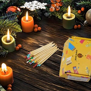 May include: A festive arrangement featuring lit candles in orange and green holders, surrounded by Christmas ornaments and greenery. A bundle of matches with colorful tips and a yellow box with the text "IGNITE EASE" are also present.